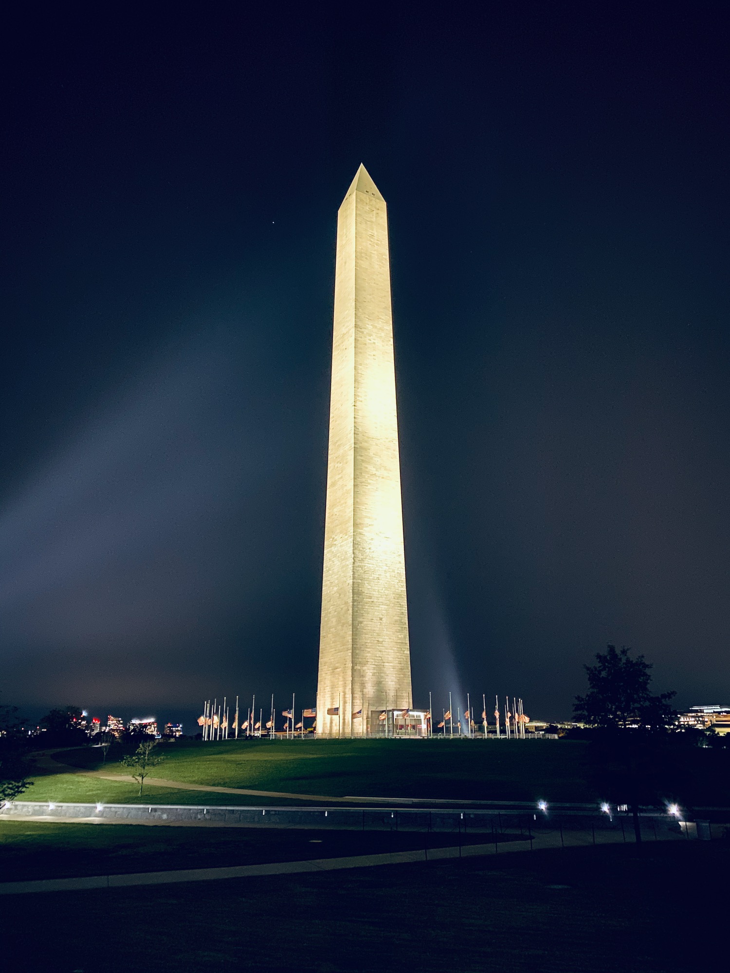 a tall tower with lights at night with Washington Monument in the background