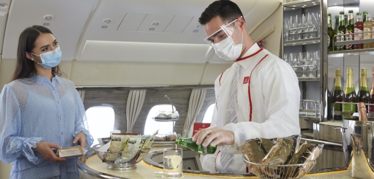 a man wearing face mask and white coat standing at a counter in an airplane
