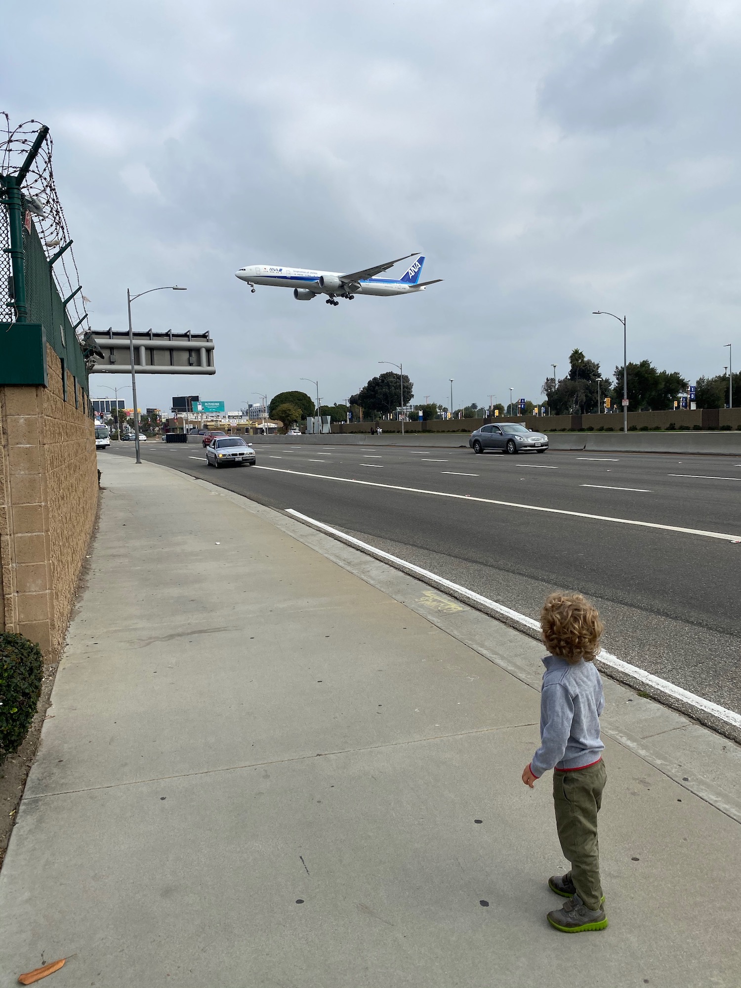 a child looking at an airplane flying over a road