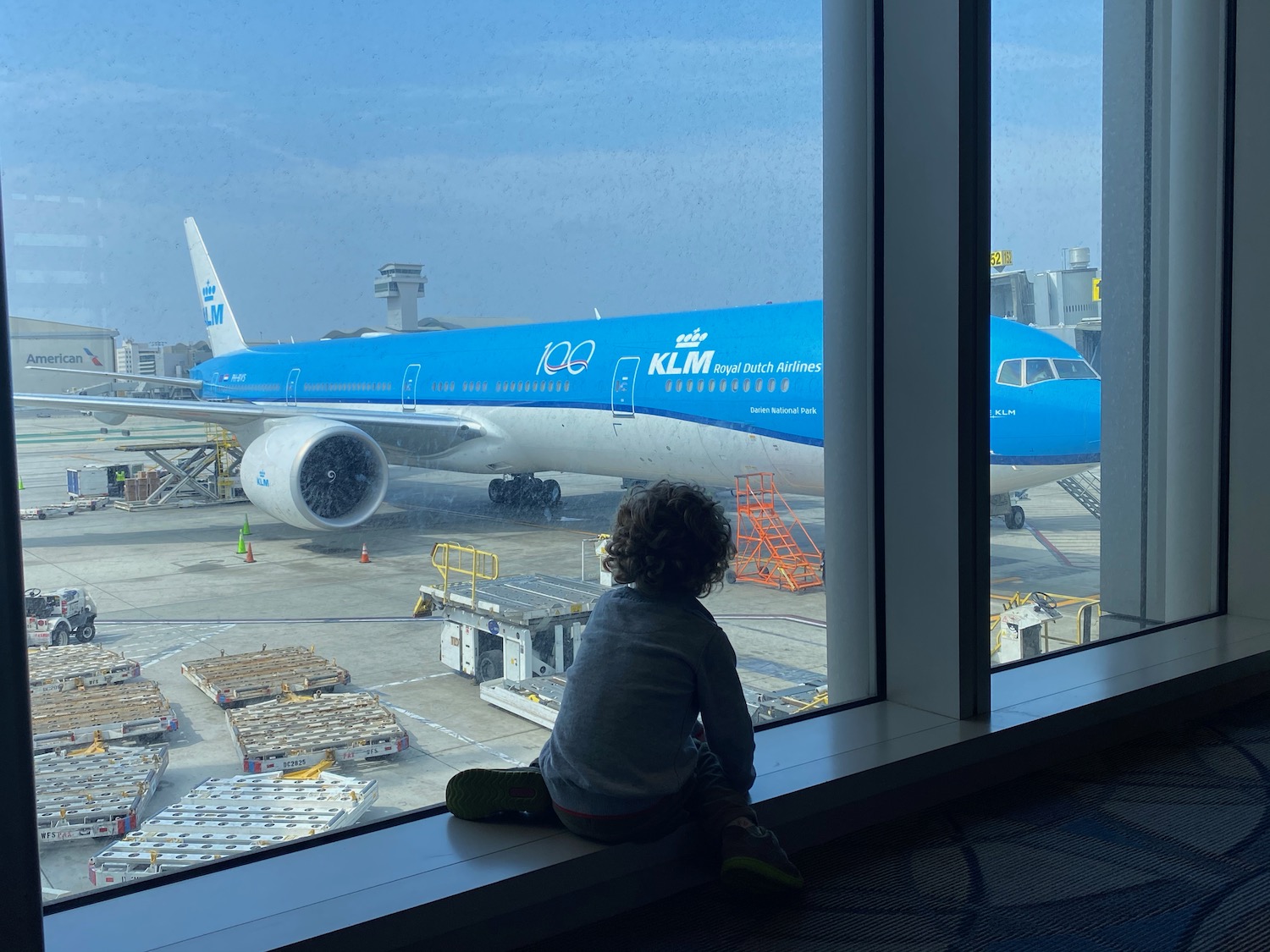 a child sitting on a window sill looking at an airplane