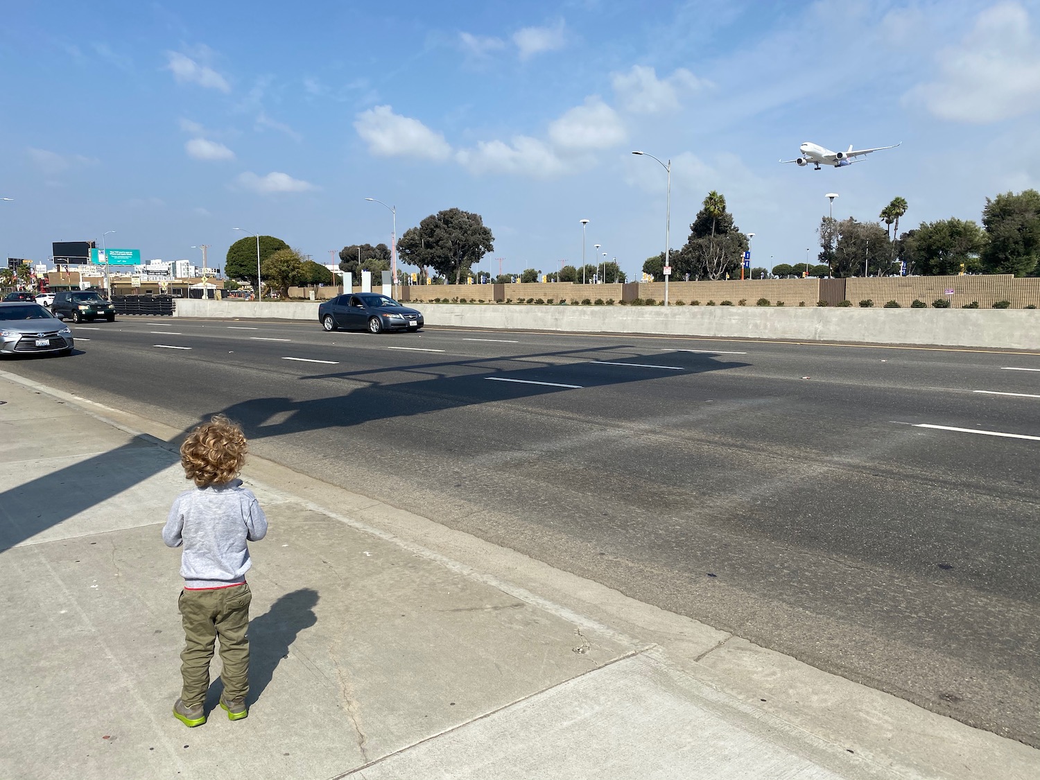 a child looking at an airplane flying over a road