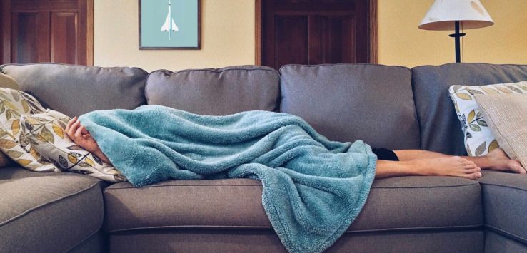 a person lying on a couch covered in a blanket