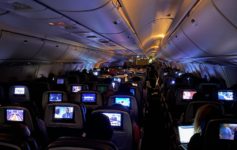 a group of people sitting in an airplane with monitors on the seats