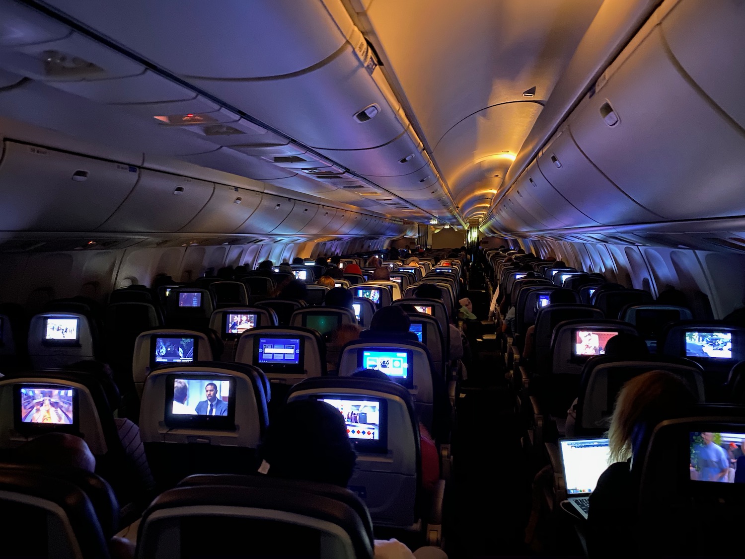 a group of people sitting in an airplane with monitors on the seats