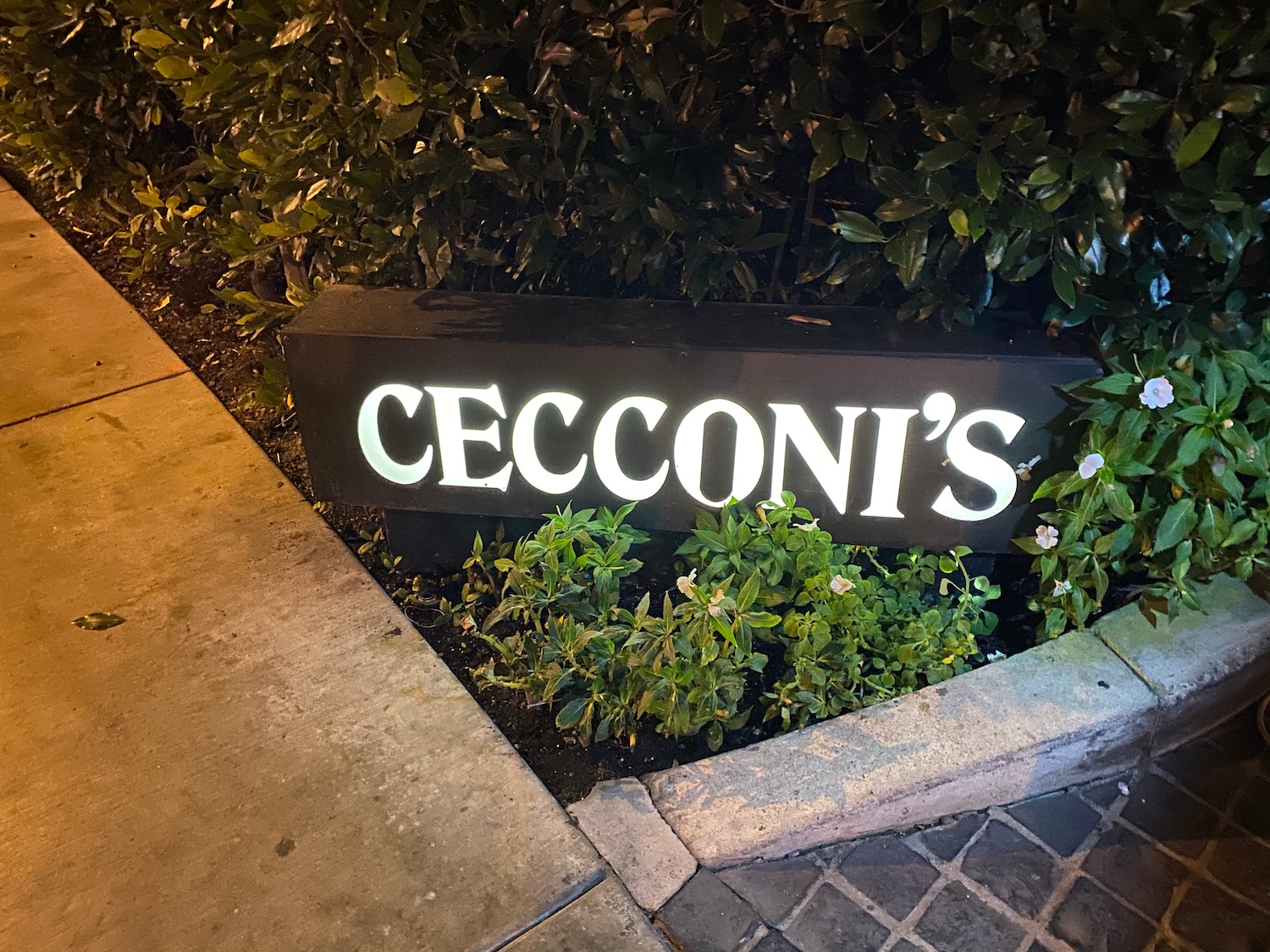 a sign with a lit up sign in front of a bush