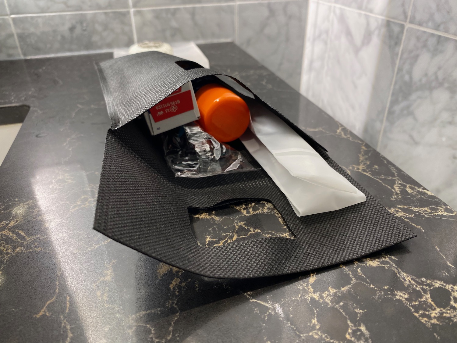 a black bag with a bottle of orange liquid and a white bag on a marble counter