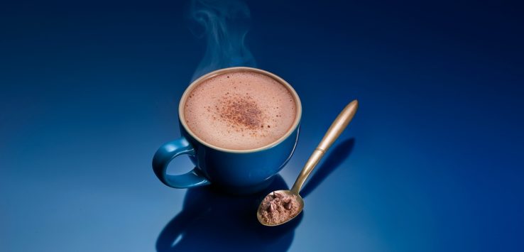 a cup of hot chocolate with a spoon and a blue background