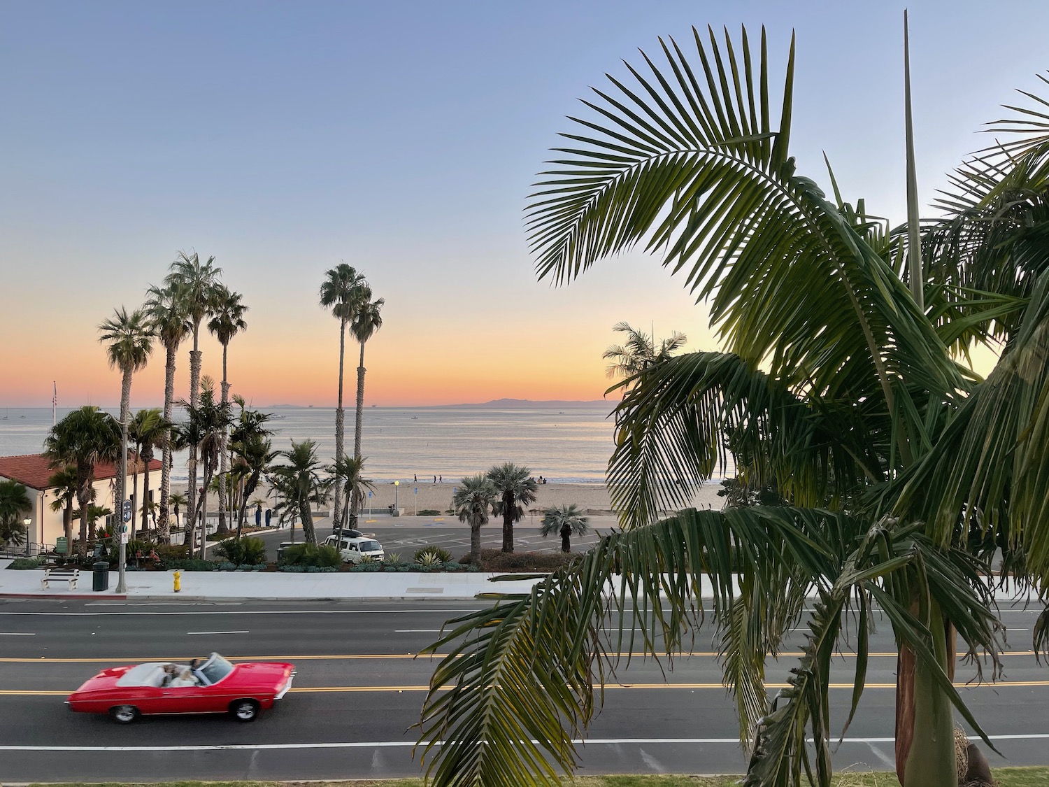 a red car driving on a road next to a beach