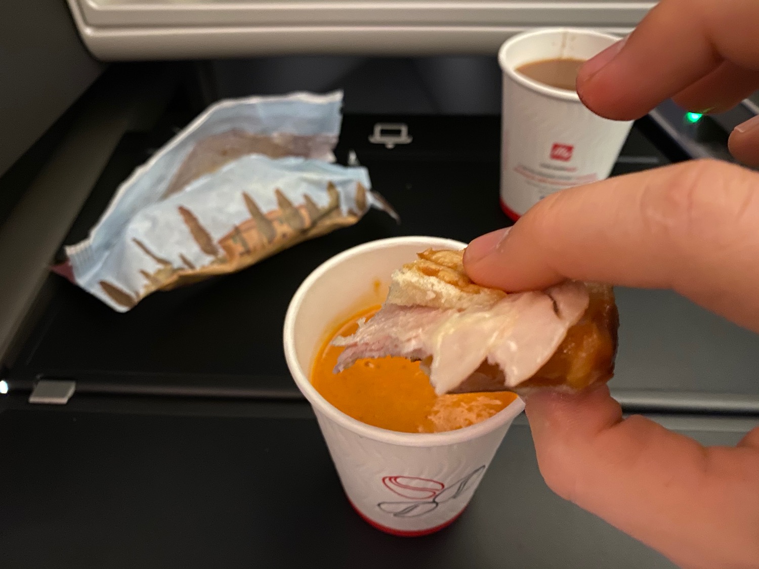 a hand holding a sandwich and a cup of soup