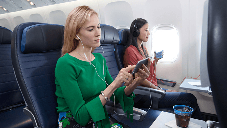 a woman sitting on an airplane with a phone and earphones