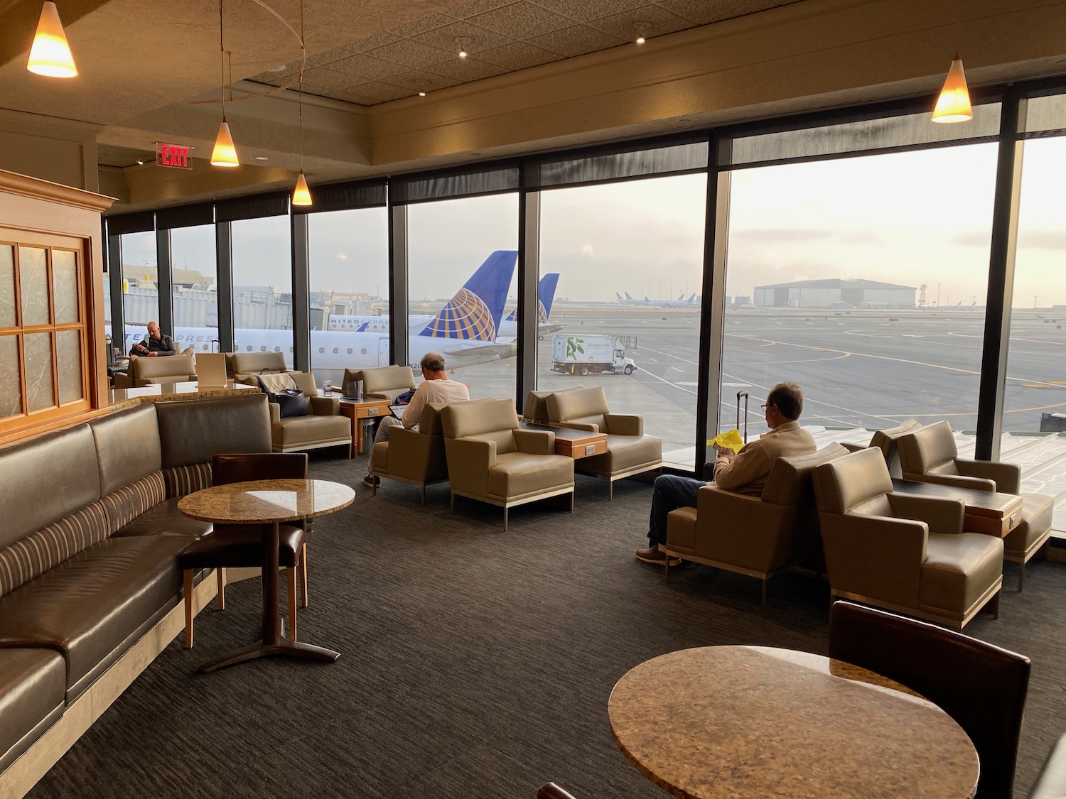 people sitting in chairs in a lounge area with large windows