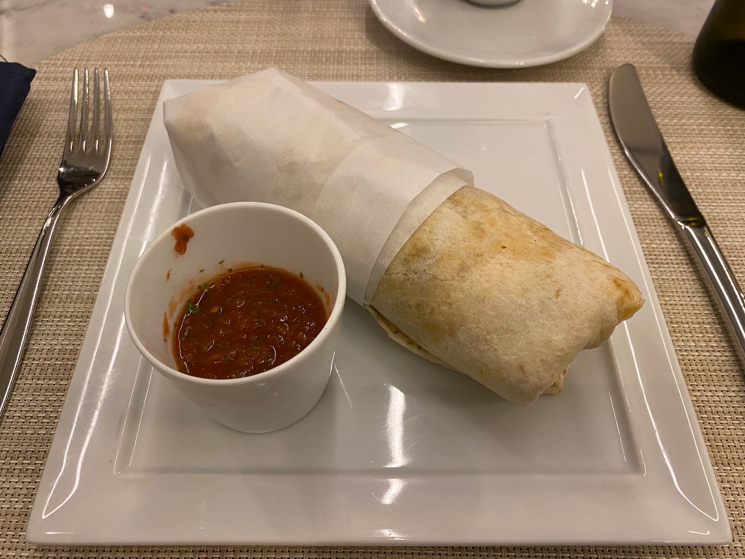 a burrito on a plate with a cup of salsa