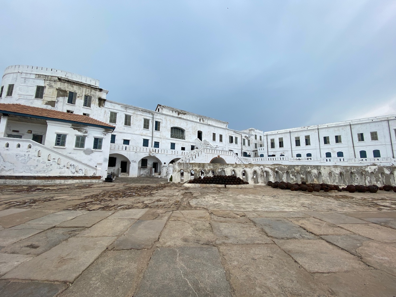 a large white building with many windows with Cape Coast Castle in the background