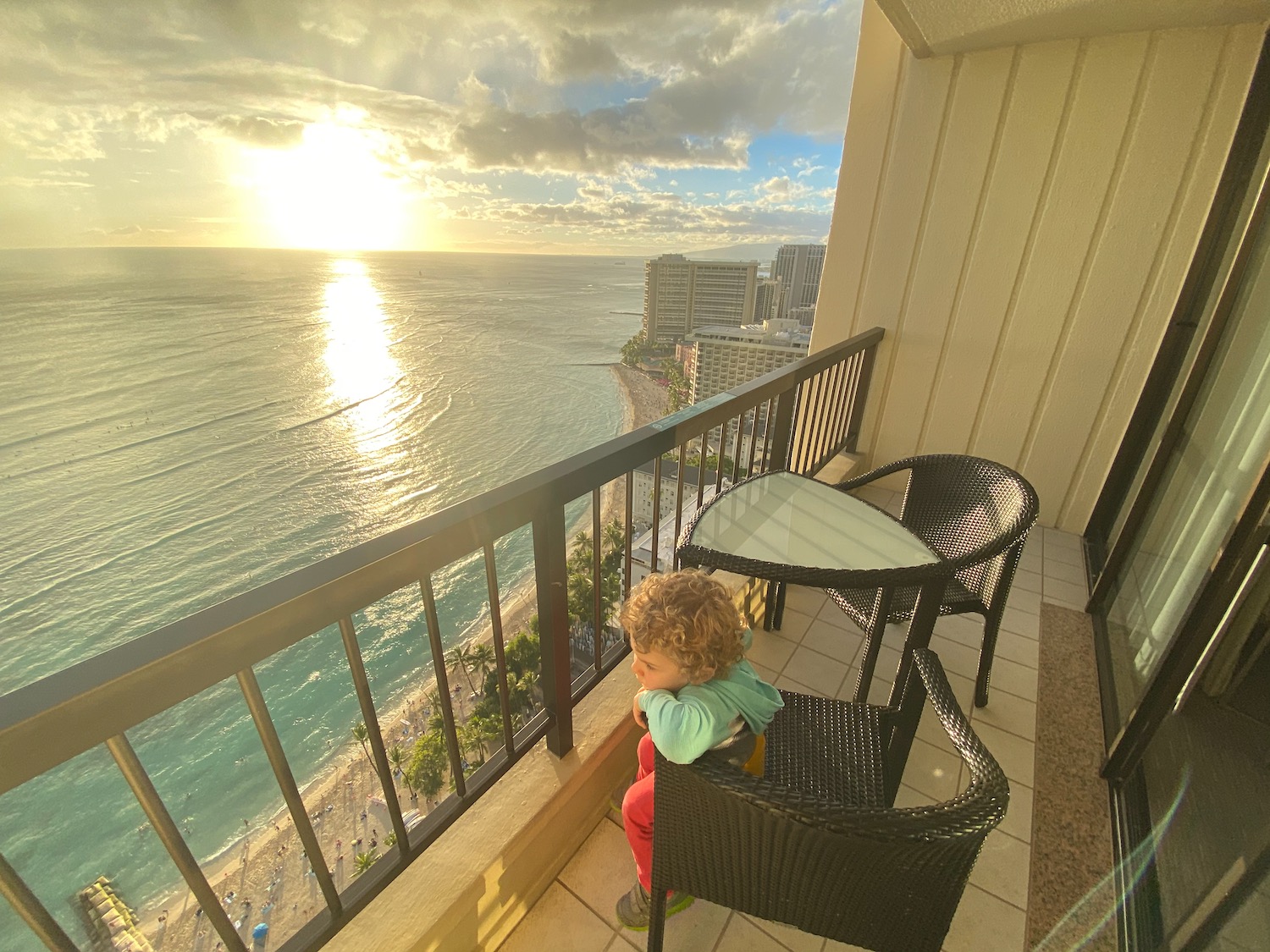 a child sitting on a chair on a balcony overlooking the ocean
