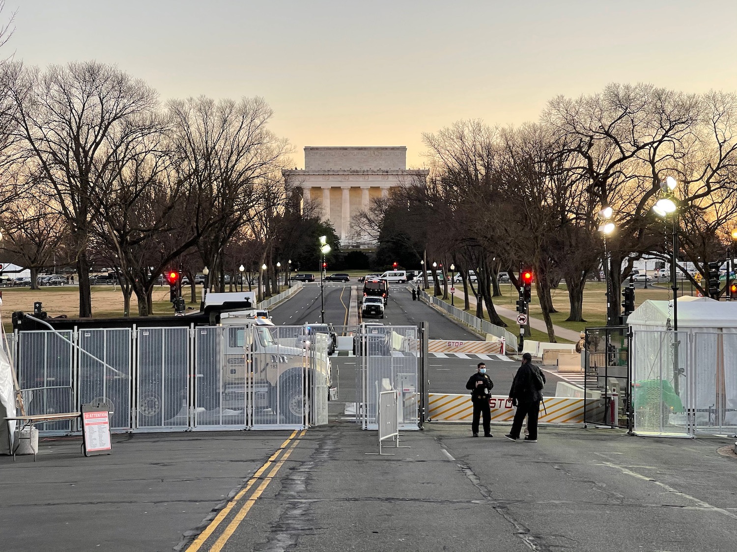 a group of people standing on a road with a fence and trees