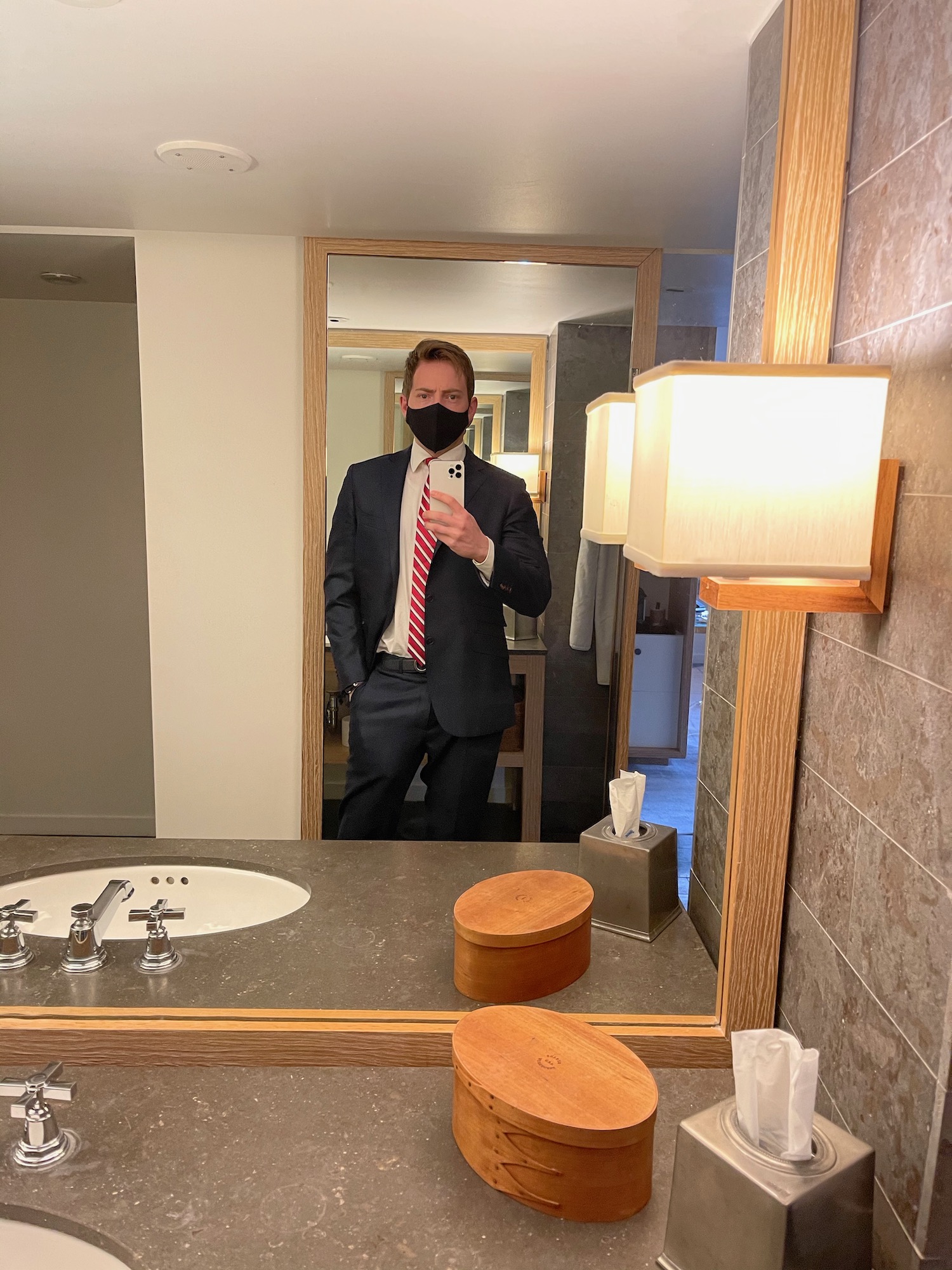 a man in a suit and tie taking a selfie in a bathroom mirror