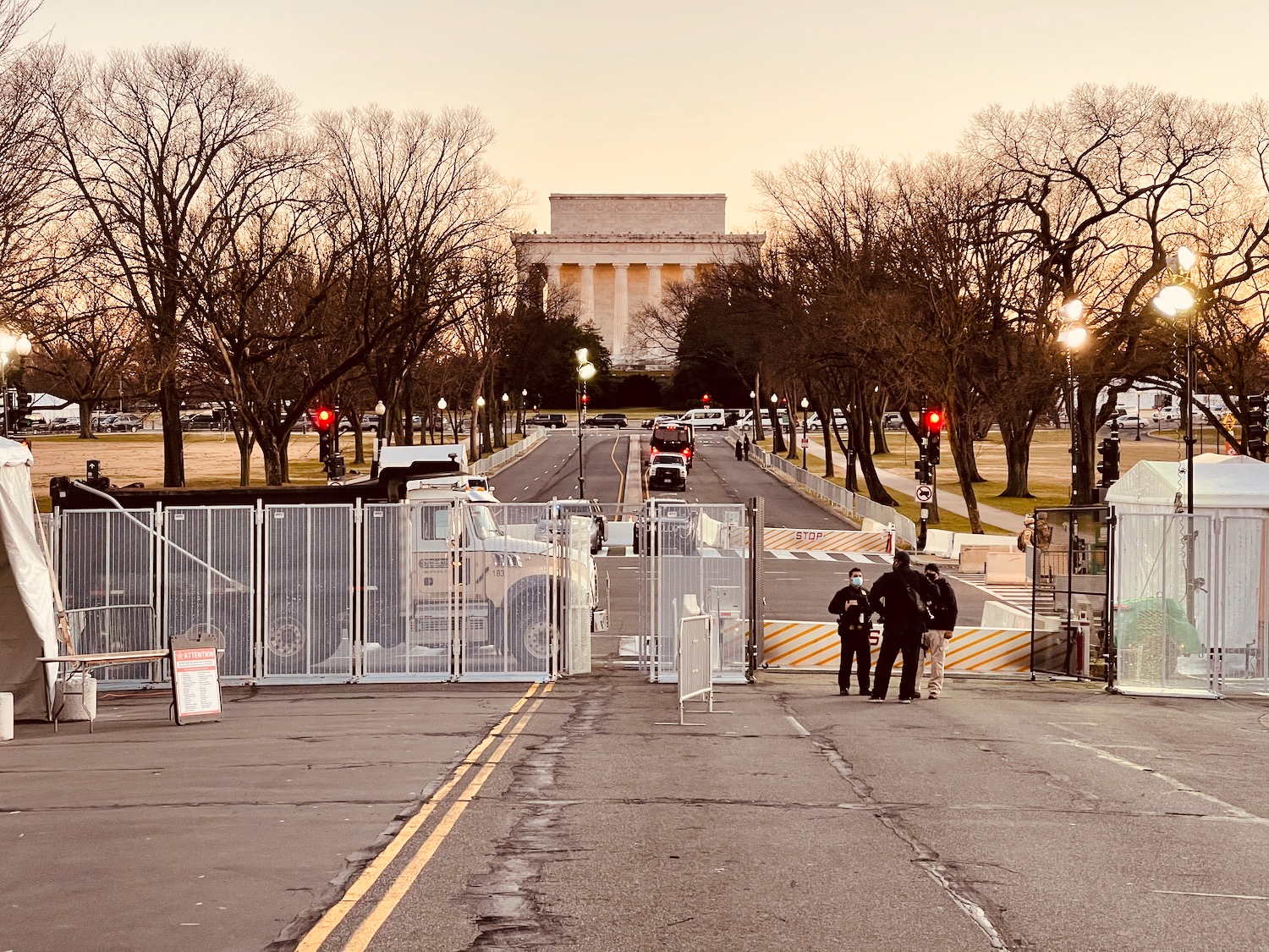 a group of people standing on a road with a fence and trees