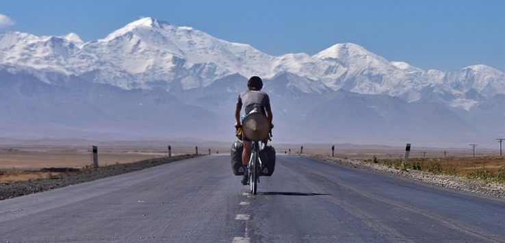 a man riding a bicycle on a road with mountains in the background