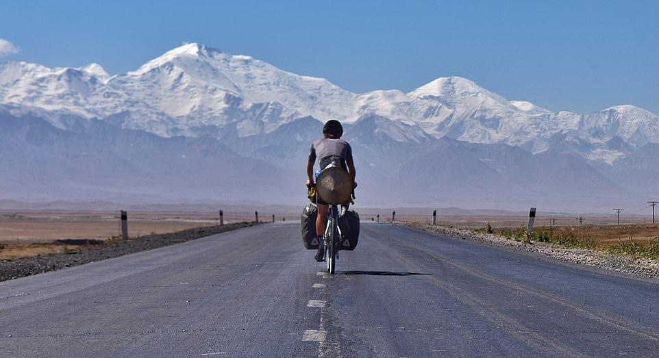 a man riding a bicycle on a road with mountains in the background
