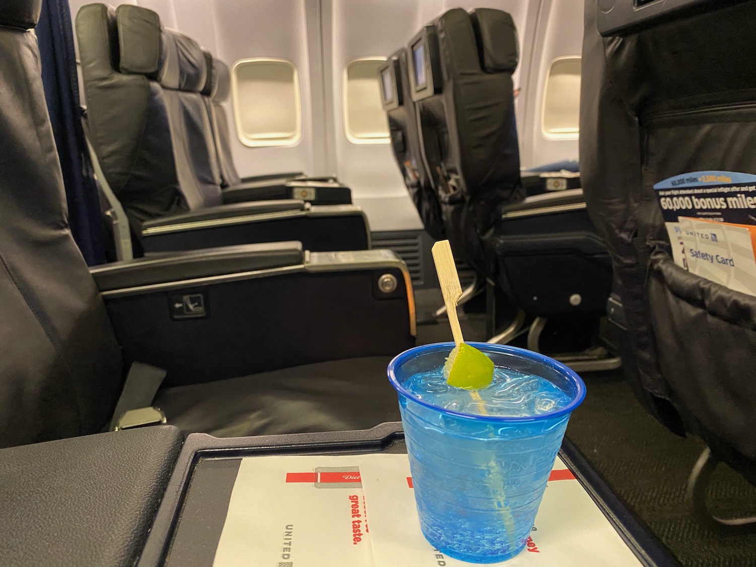 a blue drink with a lime slice on a tray in an airplane