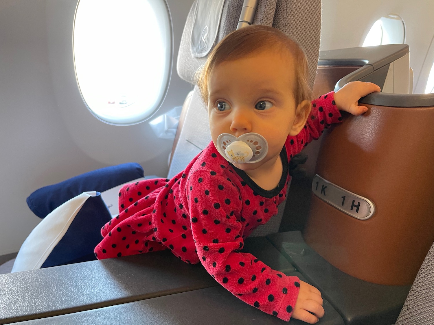 a baby in a red dress with a pacifier on the armrest of an airplane