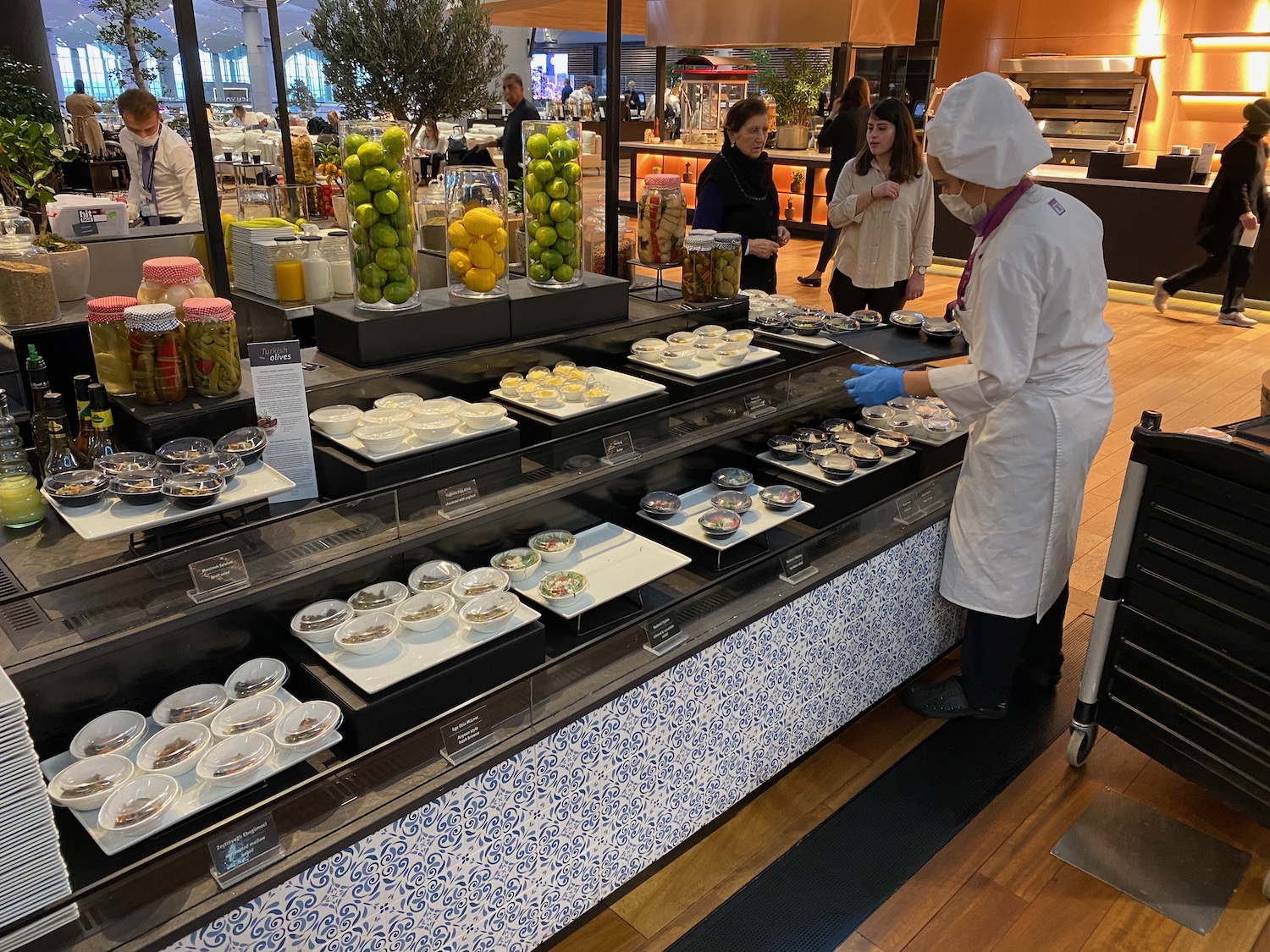 a person in a white coat and gloves standing in front of a display of food