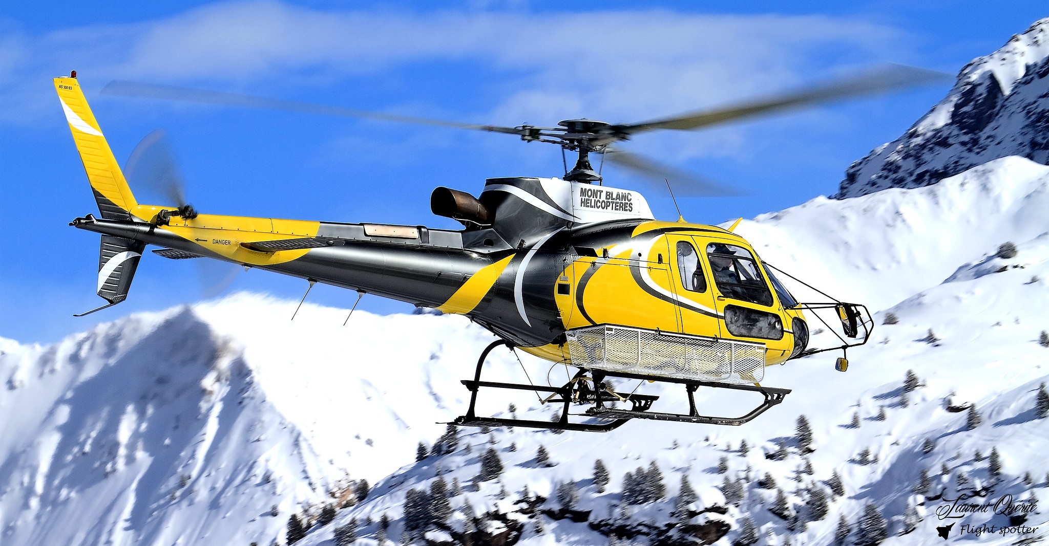 a yellow helicopter flying over snowy mountains