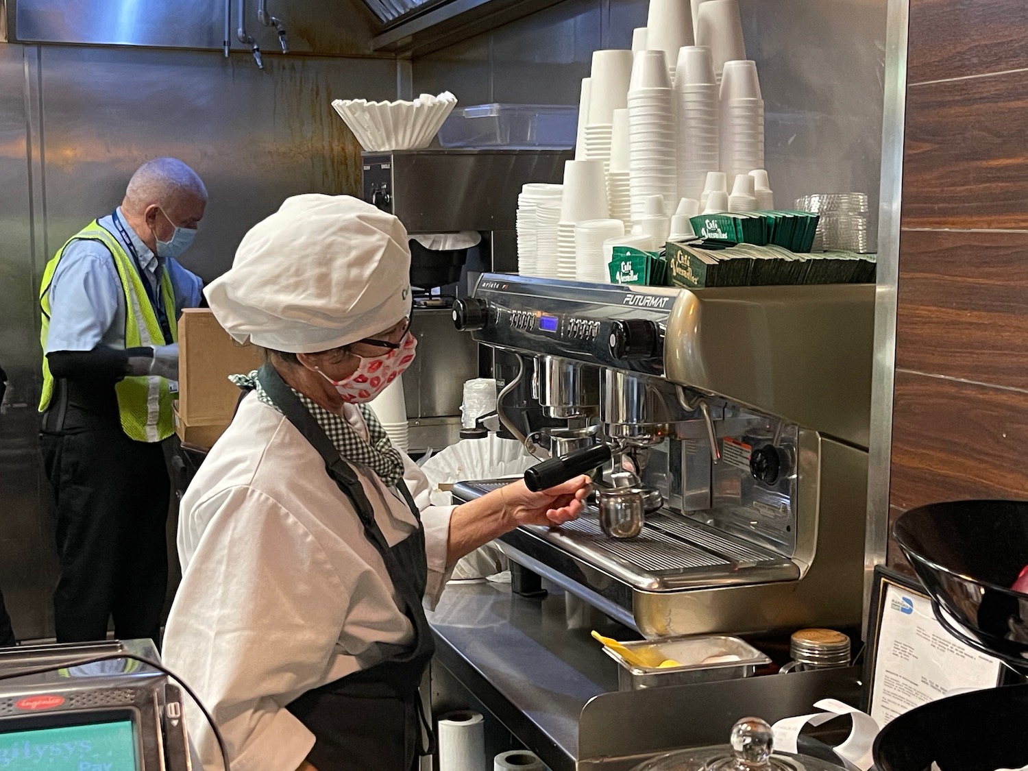 a woman wearing a mask and white hat working at a coffee machine