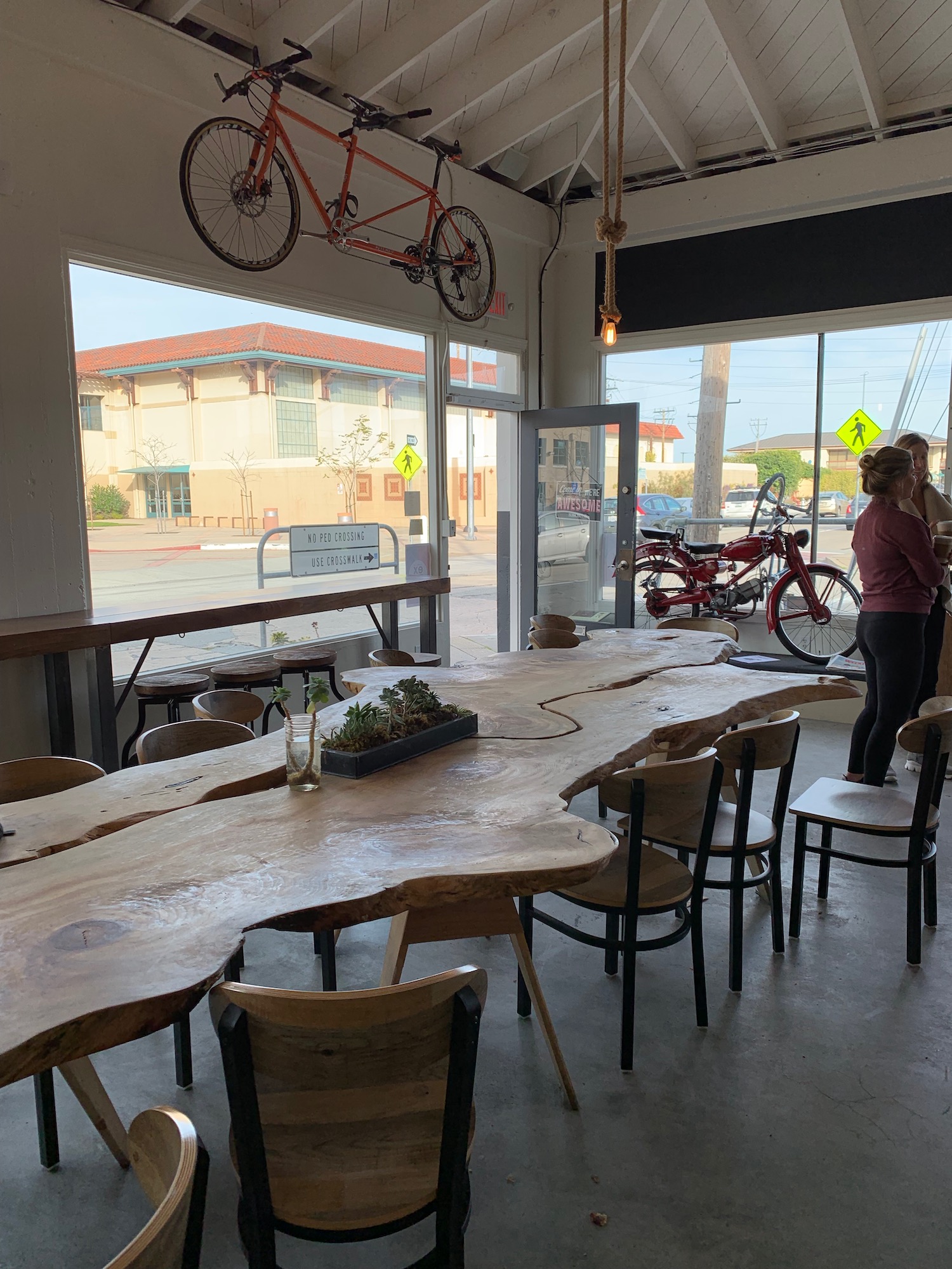 a large wooden table with chairs and a couple of people in front of a window