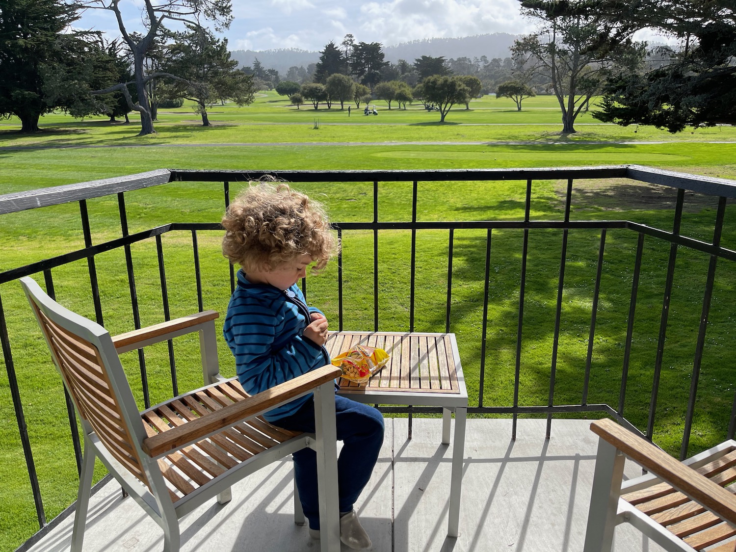 a child sitting on a chair on a deck with a table and a table with food