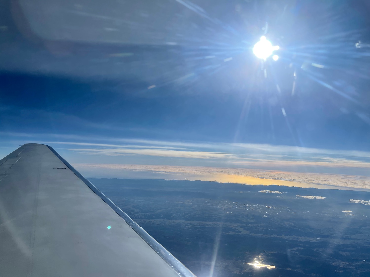 a wing of an airplane with the sun shining through the clouds