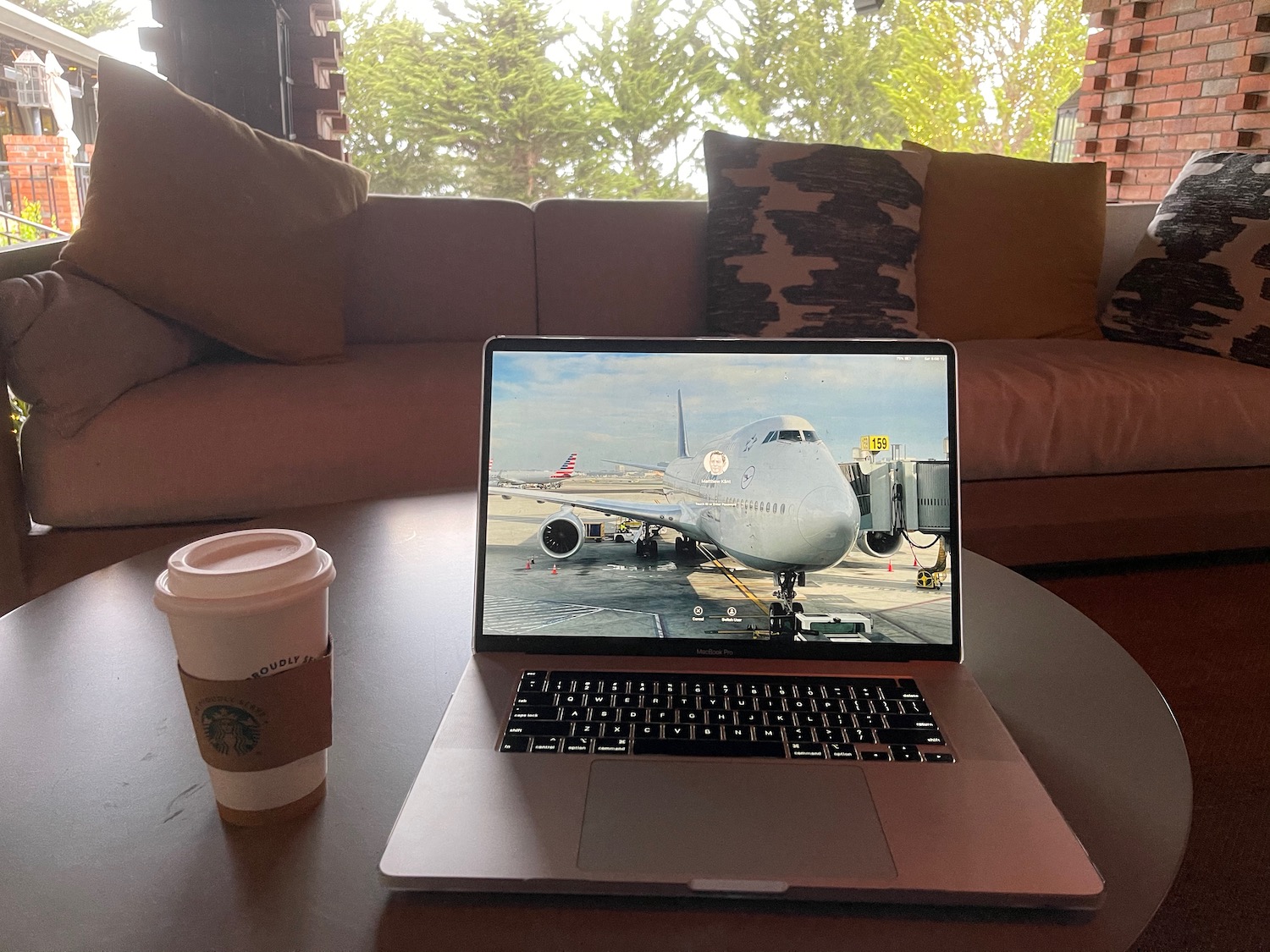 a laptop on a table with a coffee cup and trees in the background