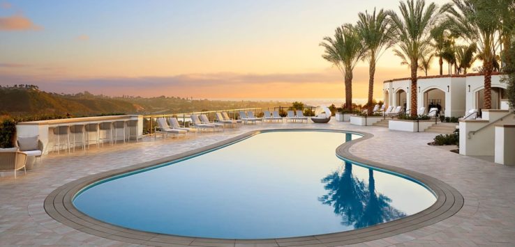 a pool with chairs and a building with a view of the ocean