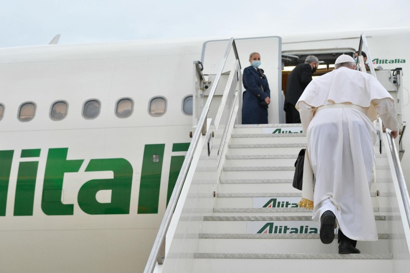 a man in white robe walking up stairs of an airplane