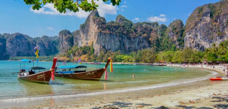 boats on a beach with rocks in the background with Railay Beach in the background