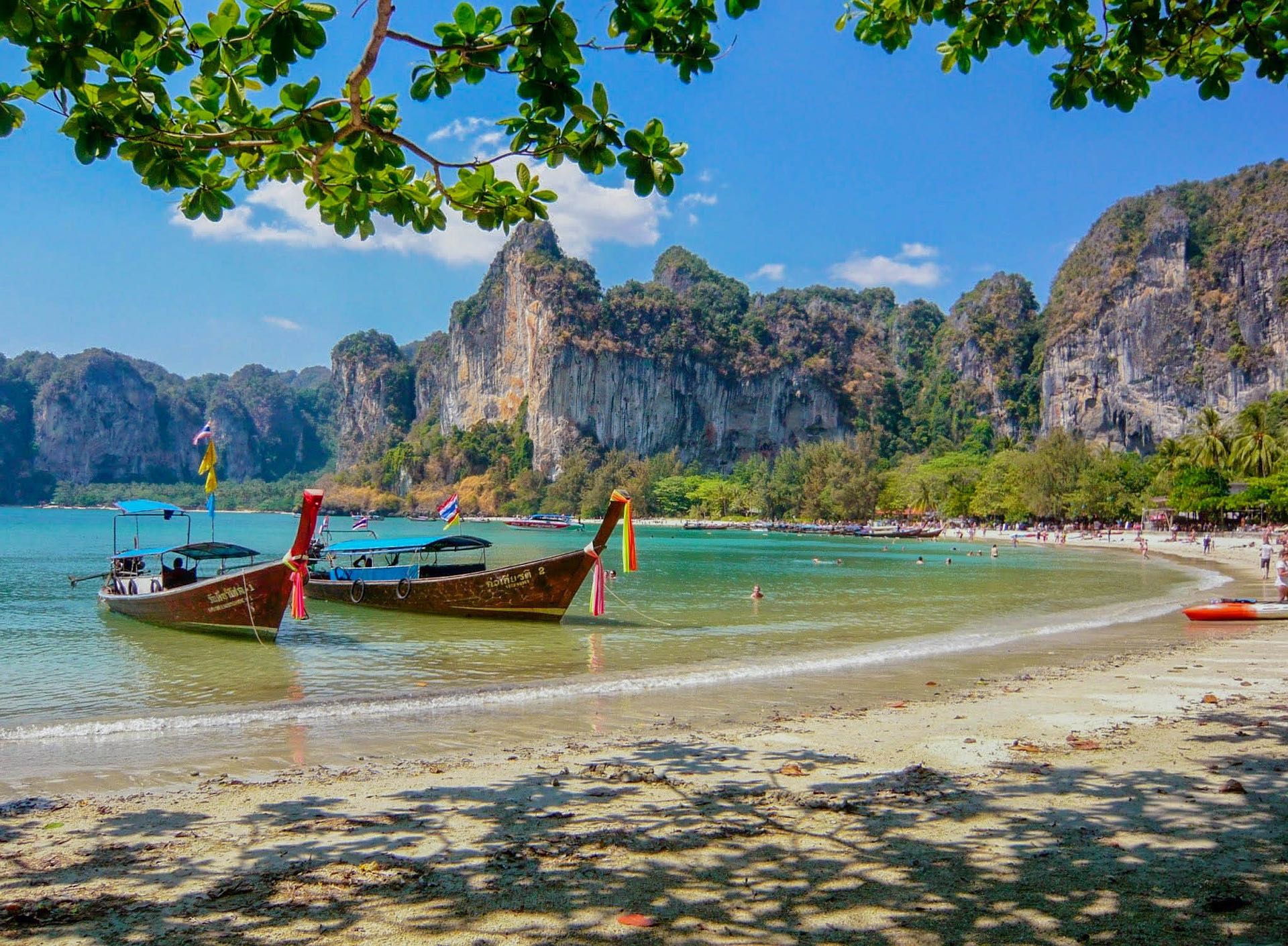 boats on a beach with rocks in the background with Railay Beach in the background