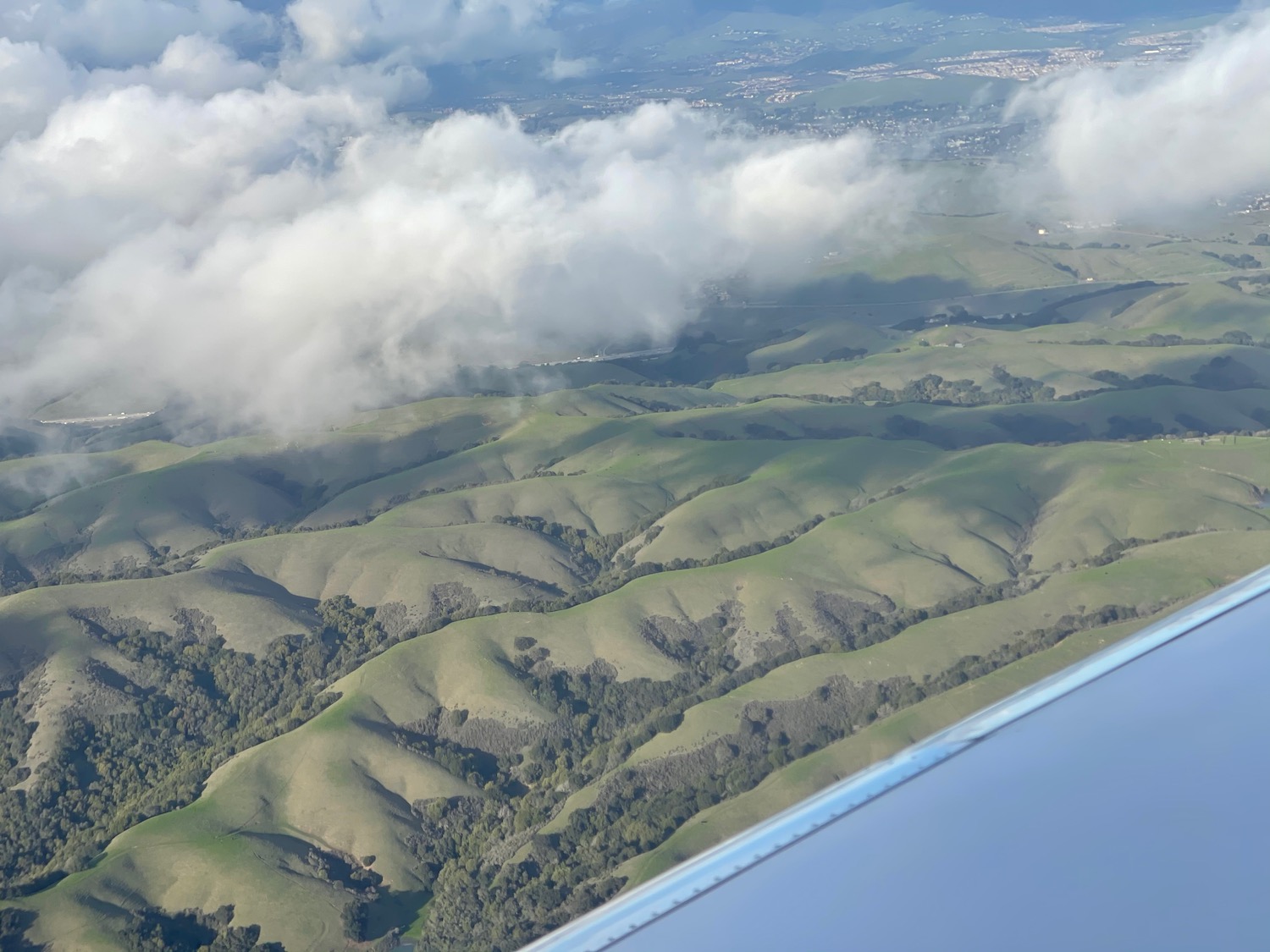 a view of a green hills and clouds from an airplane