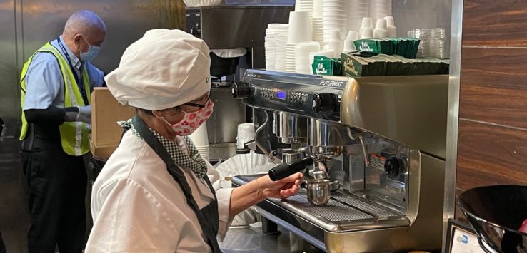 a woman wearing a mask and white hat working at a coffee machine