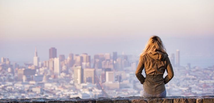 a woman sitting on a stone wall overlooking a city