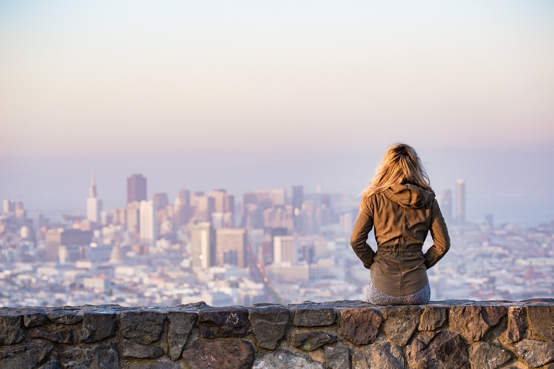 a woman sitting on a stone wall overlooking a city