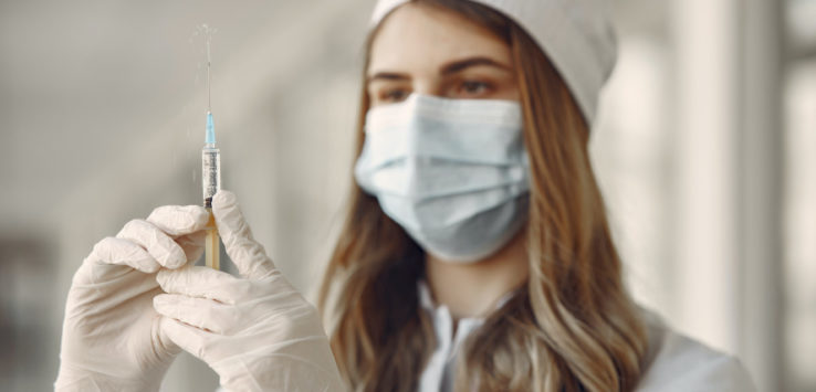 a woman wearing a mask and gloves holding a syringe