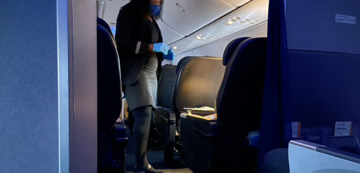 a woman wearing a face mask and gloves walking on an airplane