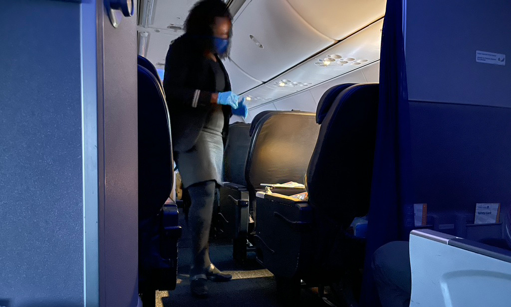 a woman wearing a face mask and gloves walking on an airplane