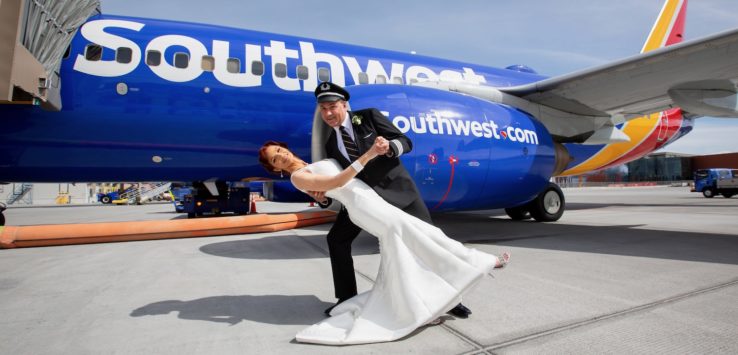 a man in a suit and a woman in a white dress in front of a blue airplane