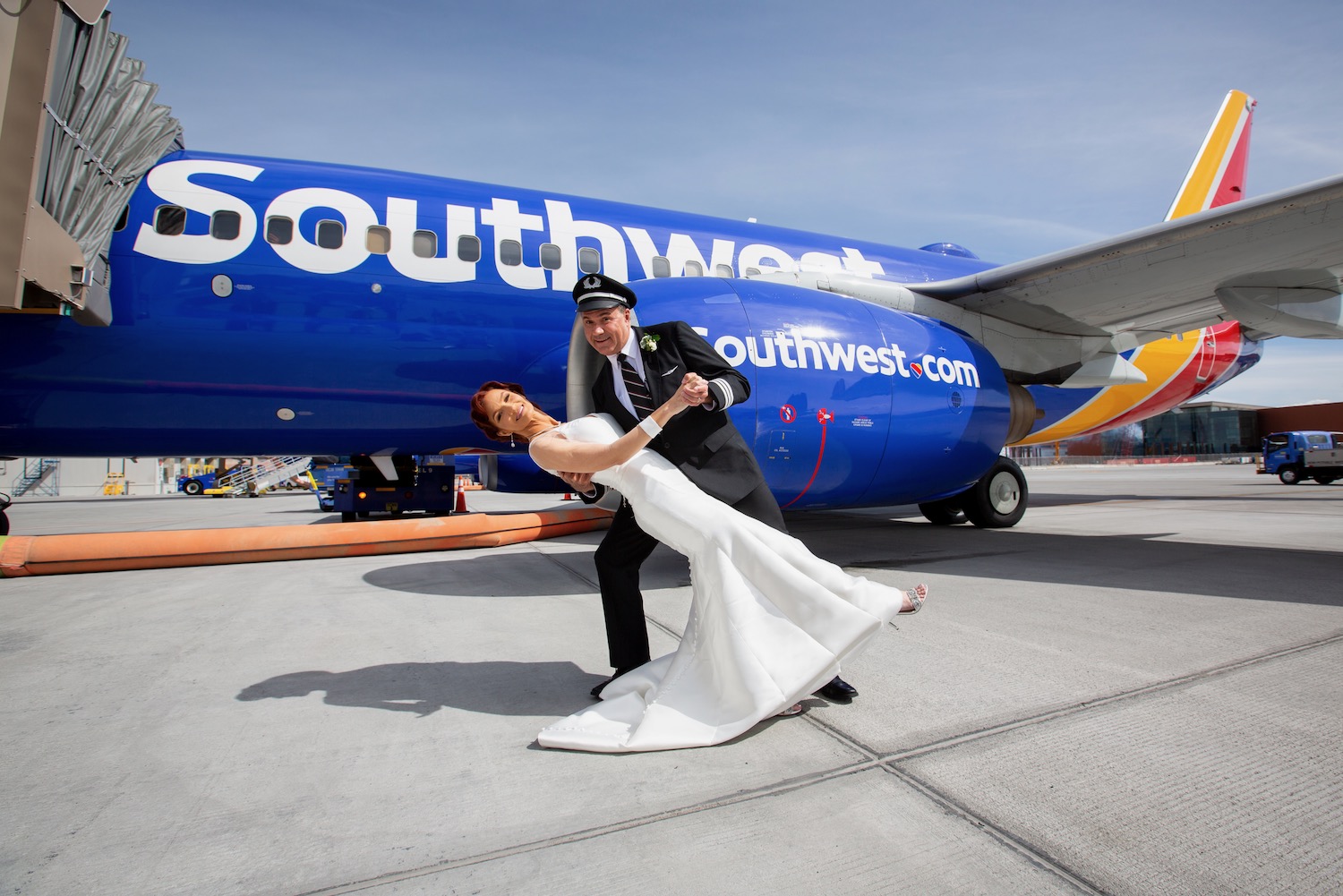 a man in a suit and a woman in a white dress in front of a blue airplane