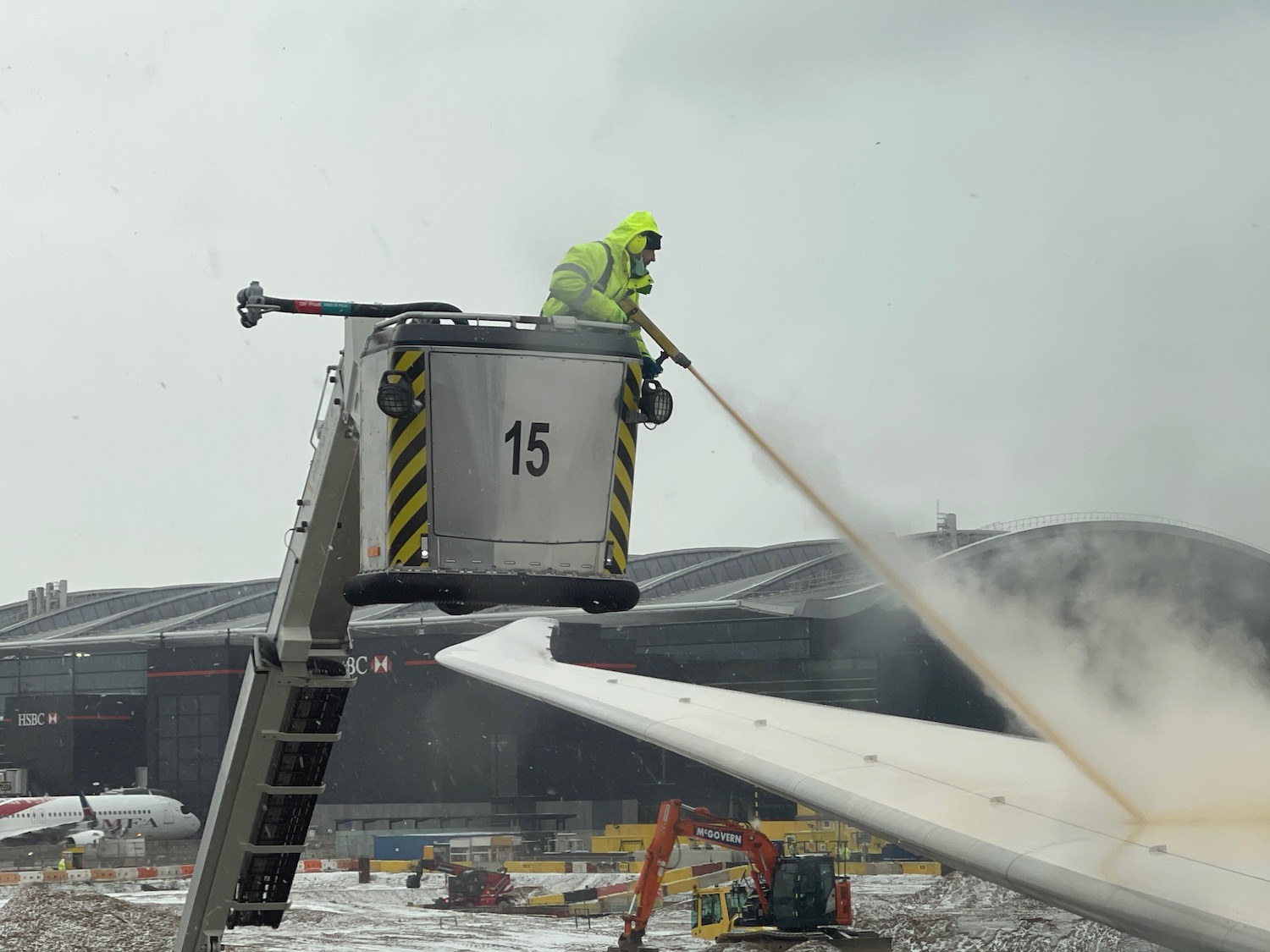 a man in a yellow jacket spraying water on a plane wing