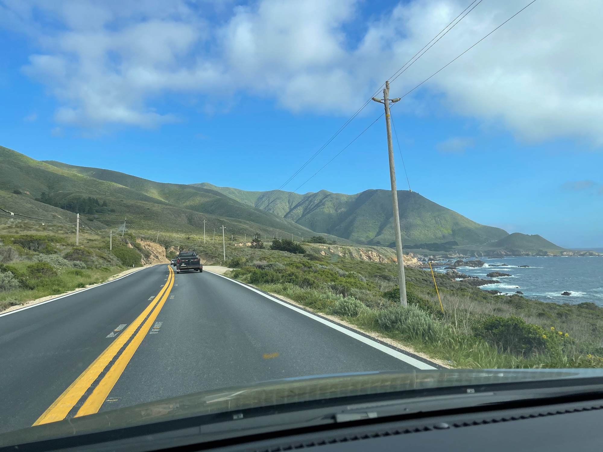 a car driving on a road with a body of water and mountains in the background