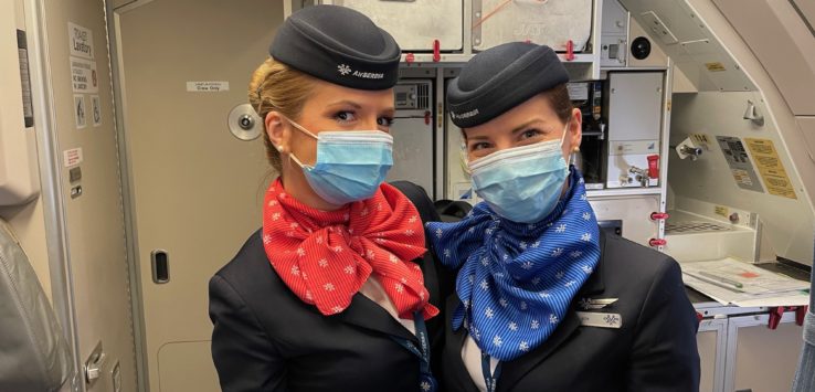 two women wearing masks and standing in a plane