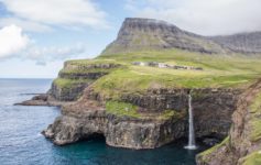 a waterfall on a cliff above water