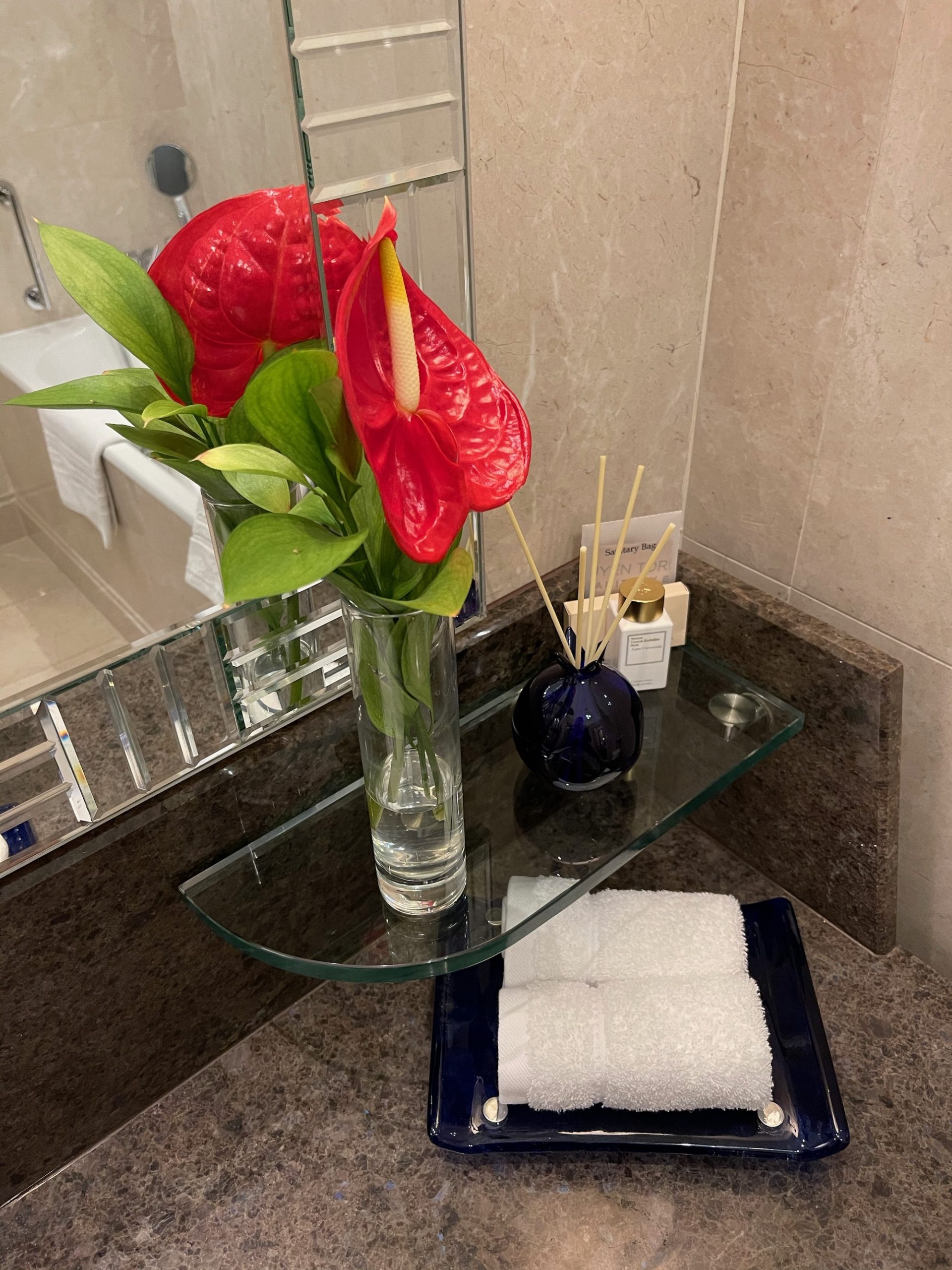 a glass shelf with a vase of flowers and a towel on it